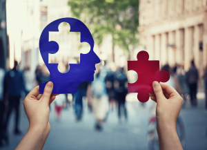  Hands holding cutouts of head and puzzle with people showing in background