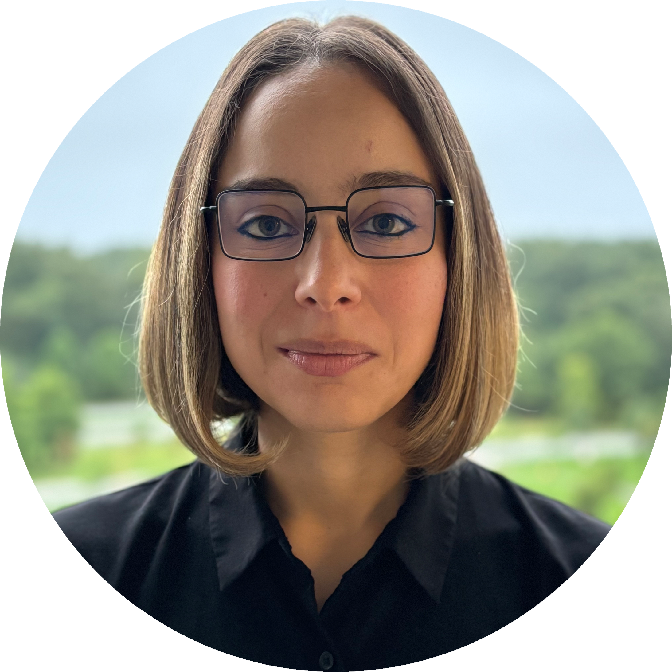 Headshot of Lina Marcella Carmona wearing glasses and a bob haircut, in a black shirt. Picture is set against a natural outdoor background