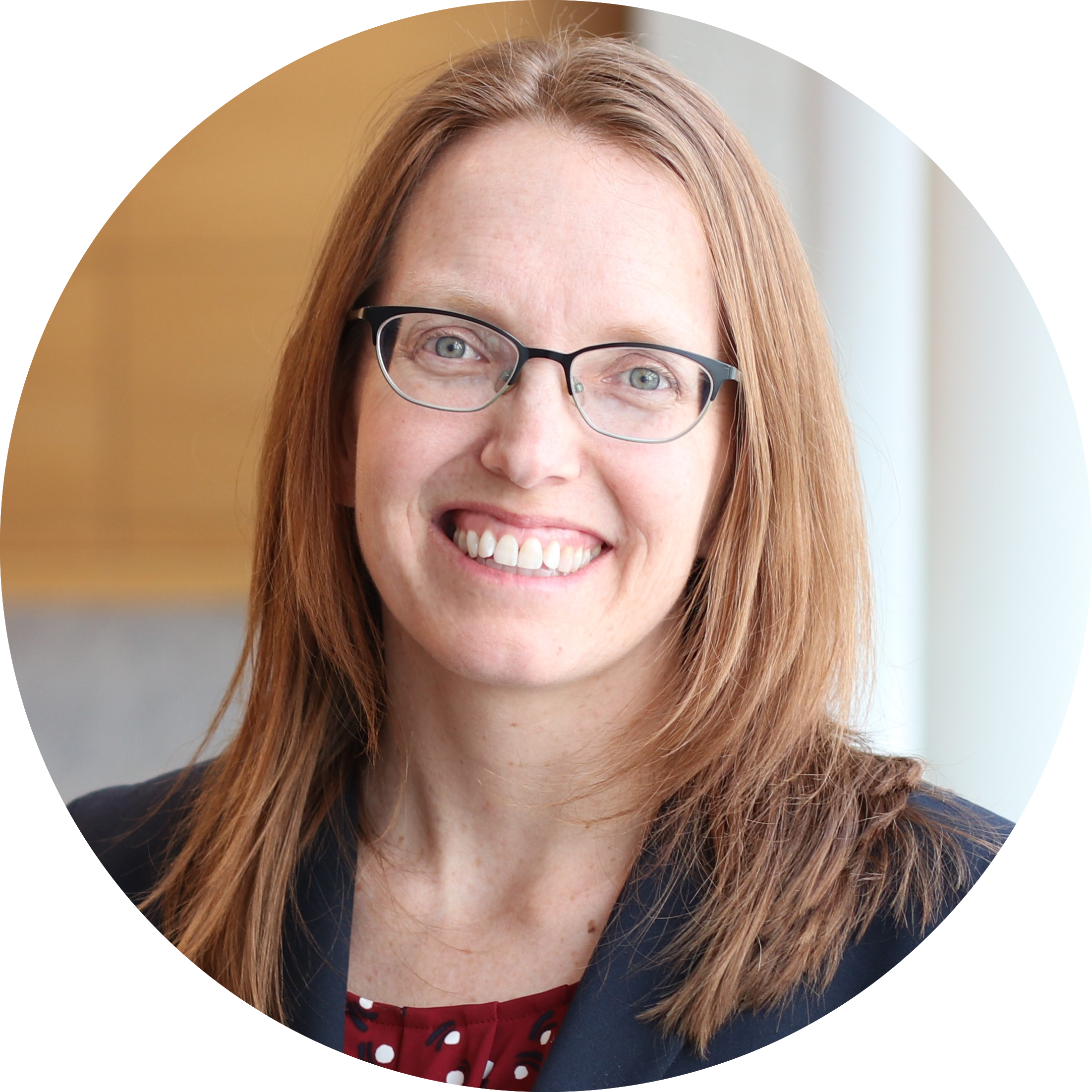 Circular portrait of Dr. Cynthia Fuhrmann, who has shoulder-length red-brown hair. She is wearing glasses and a dark blazer and is smiling