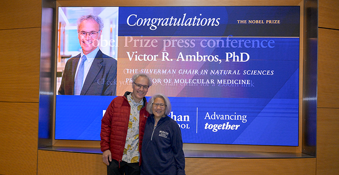 Ambros and Lee standing in front of a sign announcing the Nobel Prize.