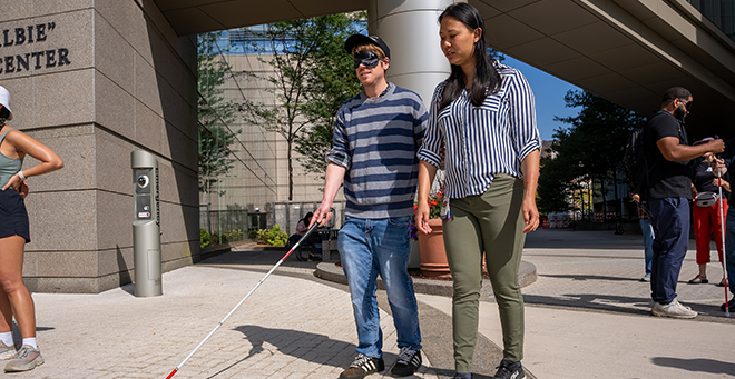 Victoria Xiao guiding blindfolded MassDOT engineer past the entrance of the Albert Sherman Center.