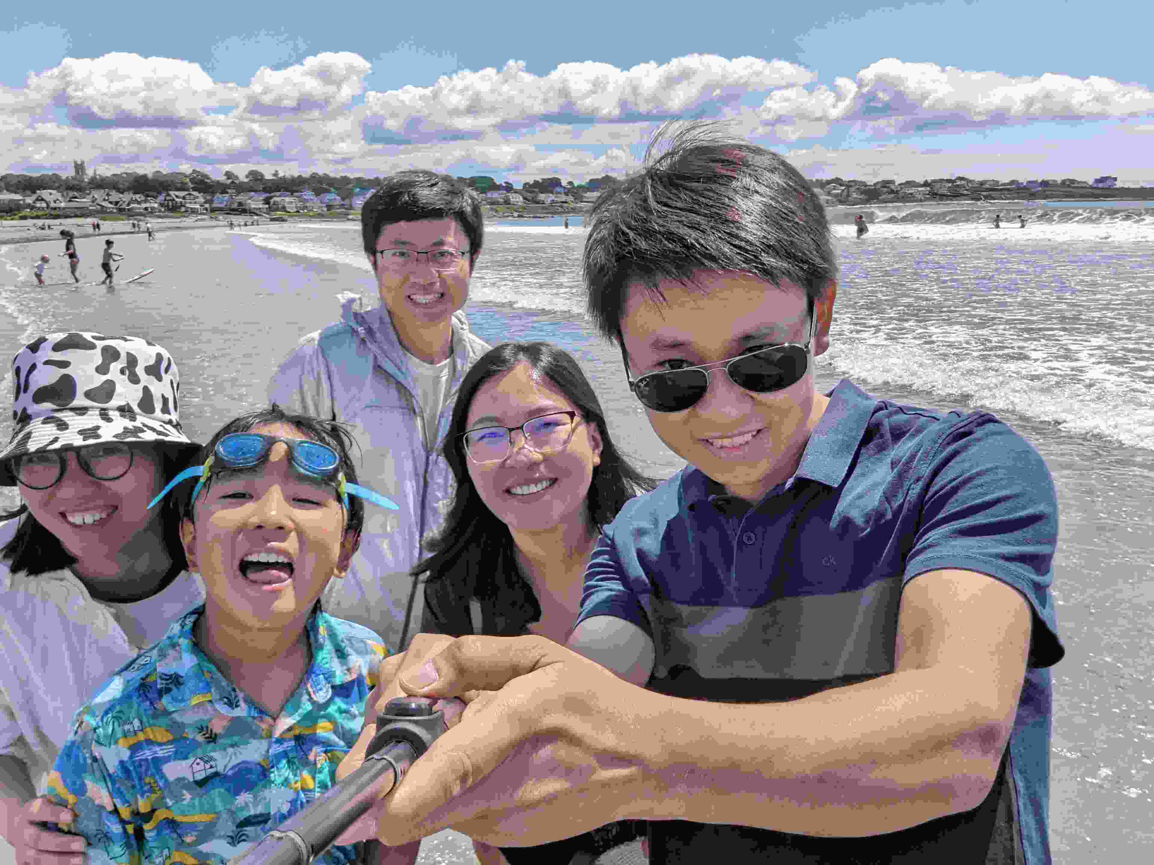 A group of five people stand on a beautiful beach, smiling for a group photo.