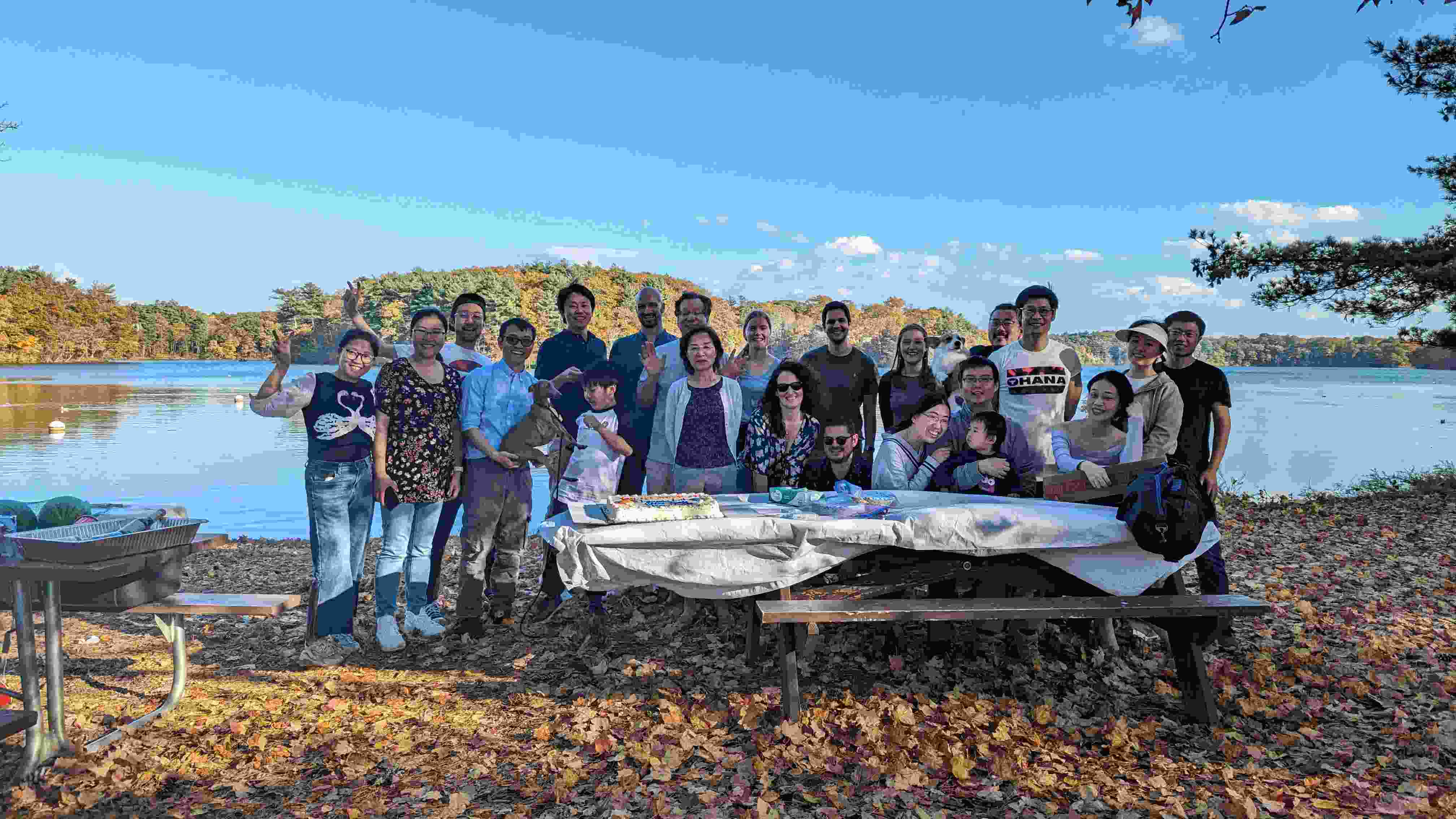 A group of 22 people standing in front of a beautiful lake, smiling for a group photo.